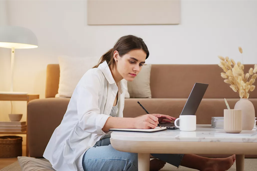 vrouw aan koffietafel aan het schrijven, laptop en kopje op tafel