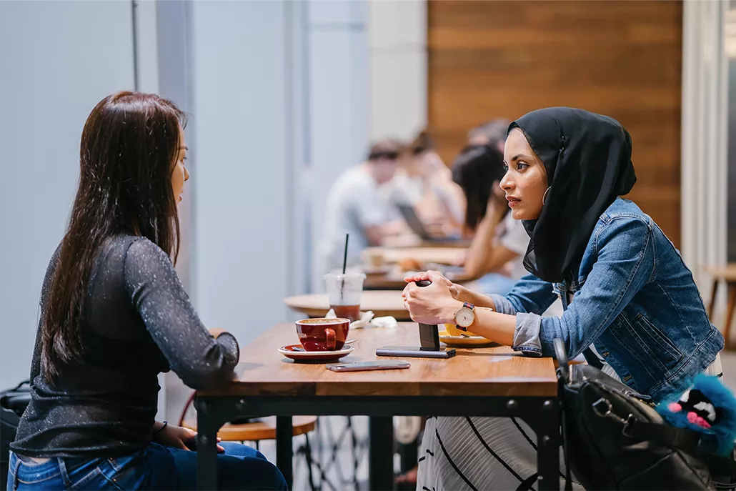 vrouw met hoofddoek samen in gesprek met ander vrouw aan tafeltje
