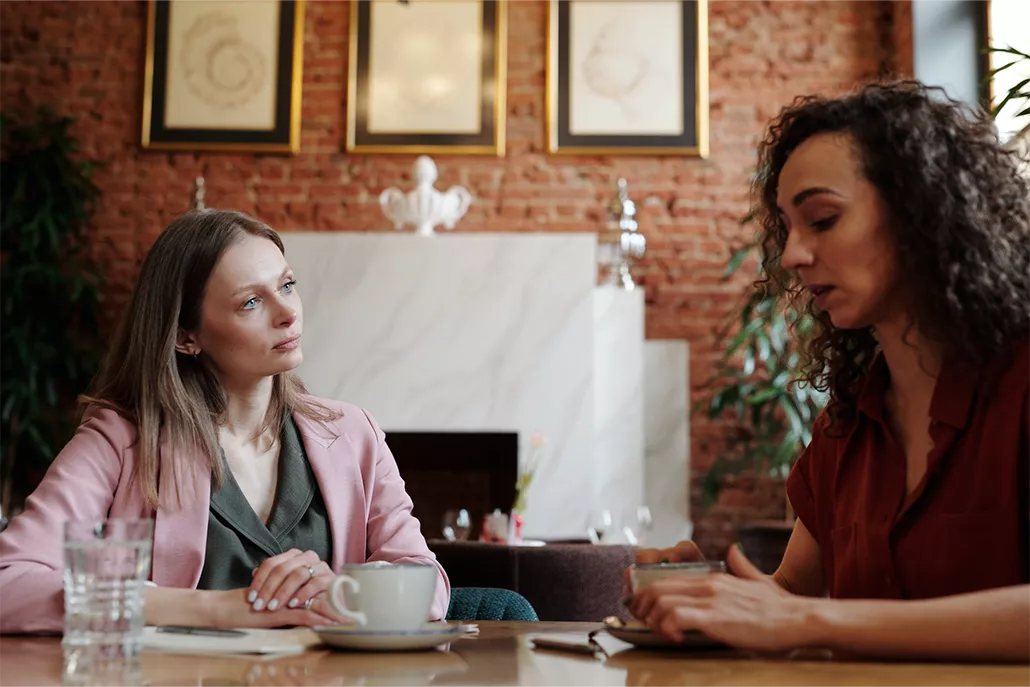 twee vrouwen aan tafel met kopjes drinken een luisterd de ander praat