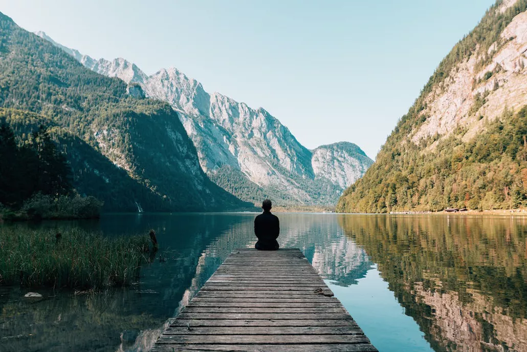 persoon mediterend op houten vlonder bij meer tussen de bergen