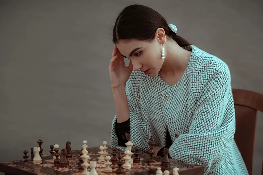 vrouw kijkend met hand tegen hoofd kijkend naar schaakbord