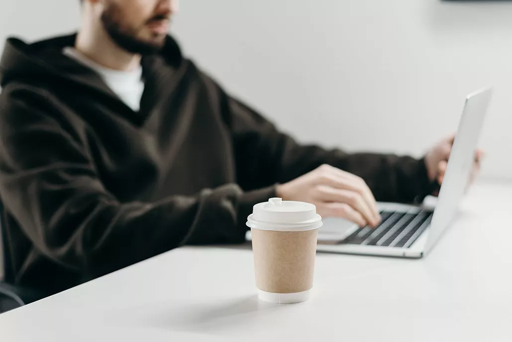 voorgrond koffie to go, achtergrond man werkend op laptop